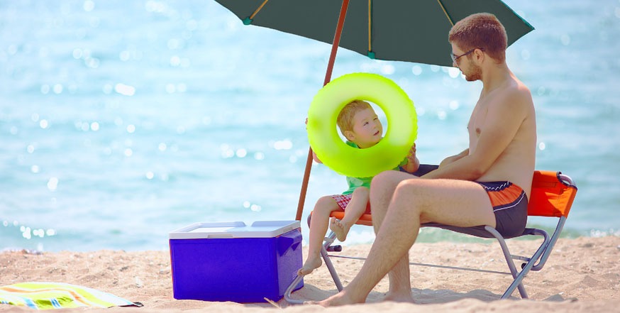 father-with-his-baby-beside-ice-cooler-in-beach-sun-shade